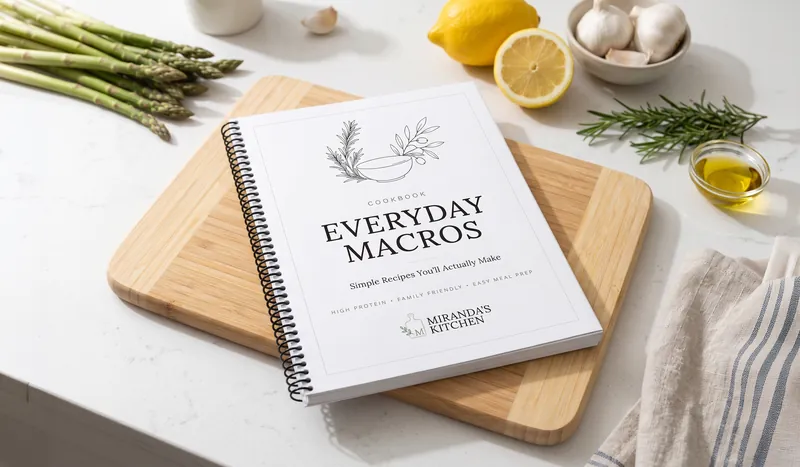 The Everyday Macros cookbook on a cutting board, with asparagus, lemon, and rosemary